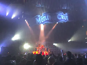 Motley Crue on a smoky stage lit by spotlights, with the band logo overhead