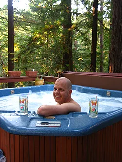 Stephen grinning in the backyard hot tub with drinks on the rim