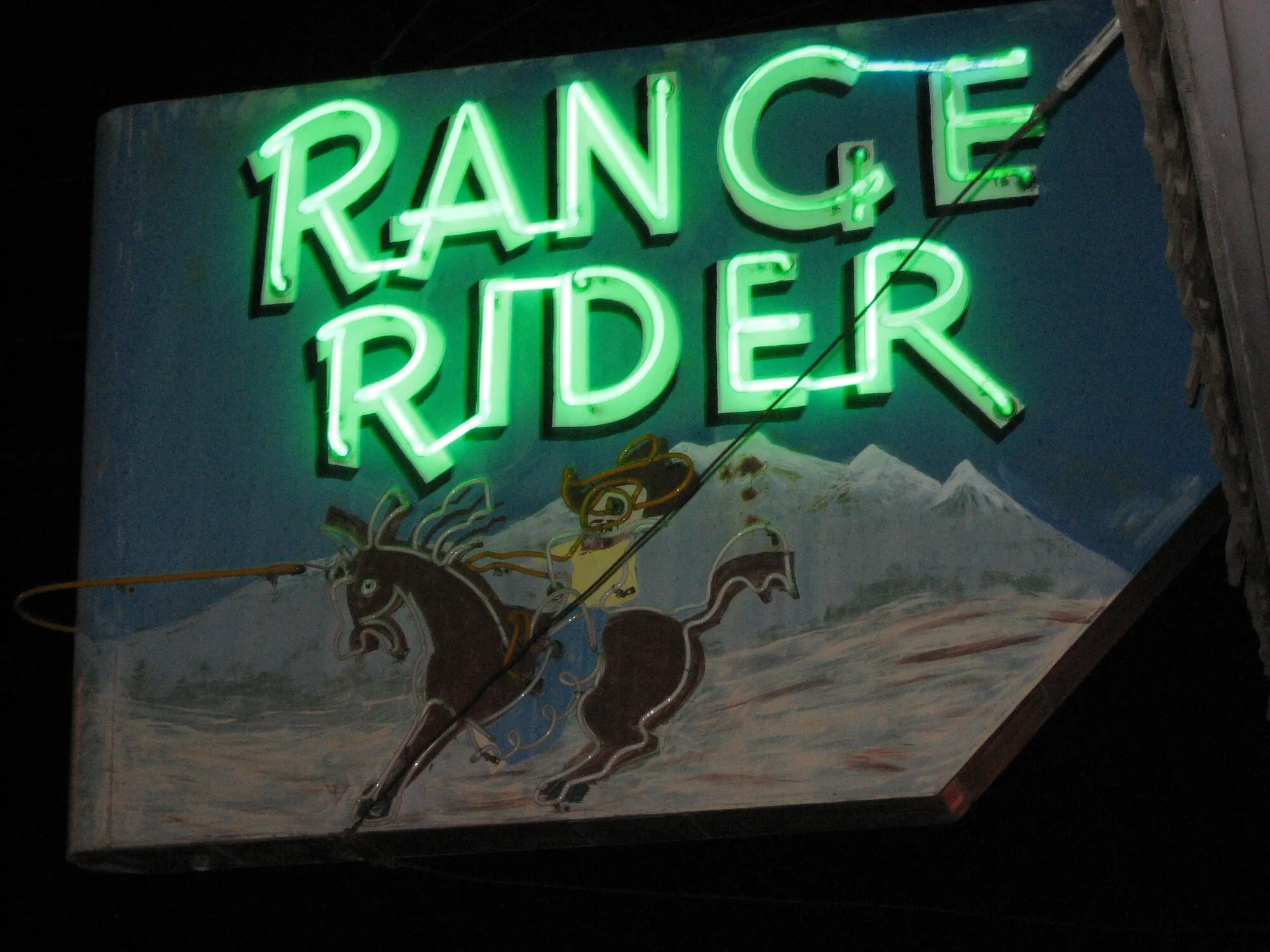 Green neon Range Rider bar sign with a cowboy on a bucking horse, lit at night